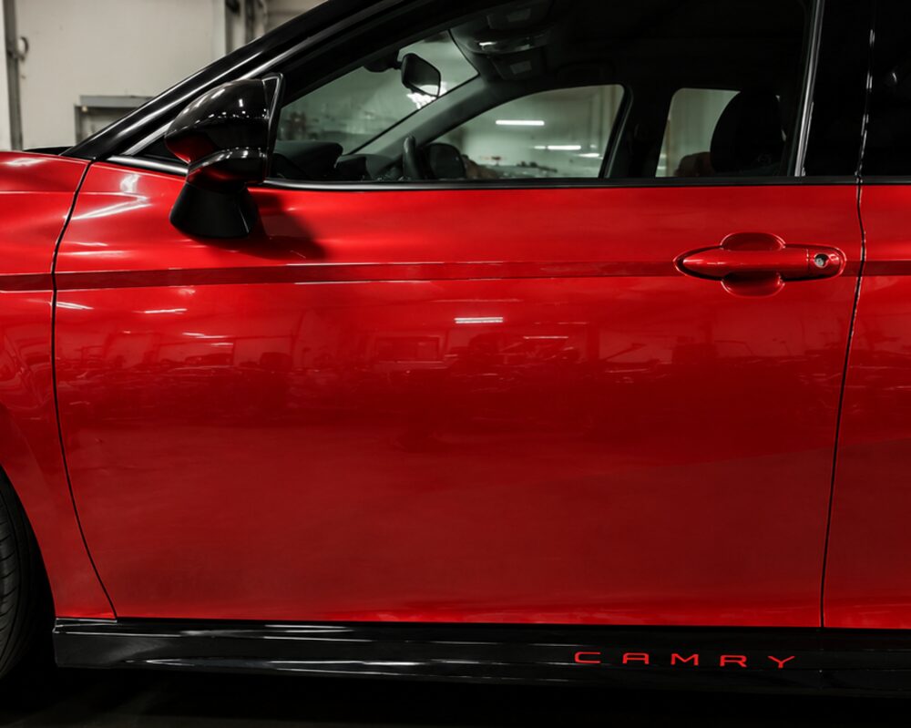 The same red Toyota Camry after collision repair, with the door line straight and the paint blended